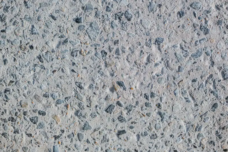 Close-up of an exposed aggregate concrete surface showing gray and dark stones in the cement paste