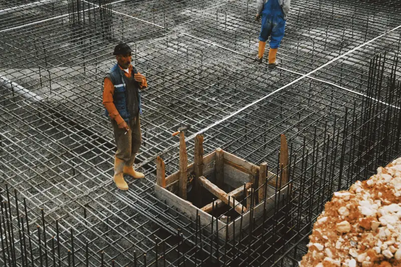 Workers on a tied rebar grid with formed openings, ready for a foundation pour