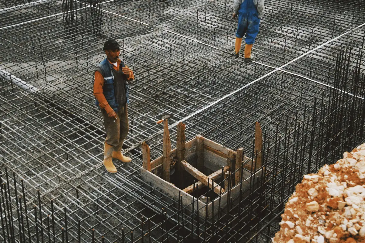 Workers on a tied rebar grid with formed openings, ready for a foundation pour