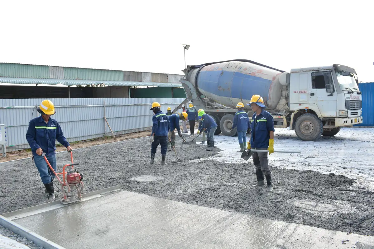 Commercial flatwork crew in hard hats spreading and screeding concrete from a mixer truck