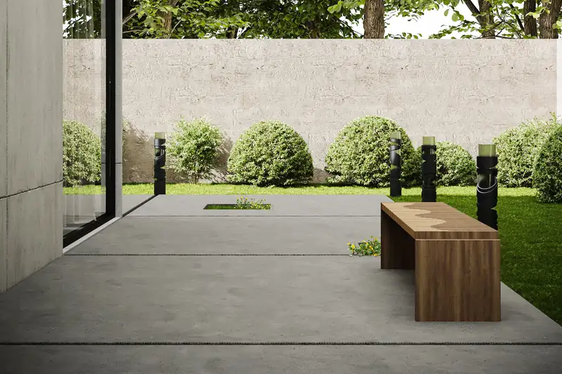 Smooth gray concrete patio with tooled joints, a wooden bench and a lawn edge beside the house